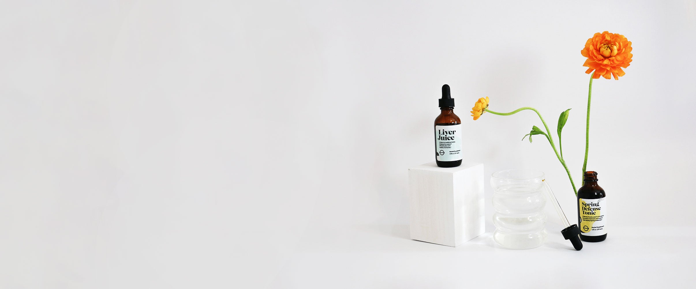 Front view of Spring Defense Tonic and Olivia’s Fave Liver Juice 2 fl oz bottles showing amber dropper bottles, open dropper and orange flowers on a white background