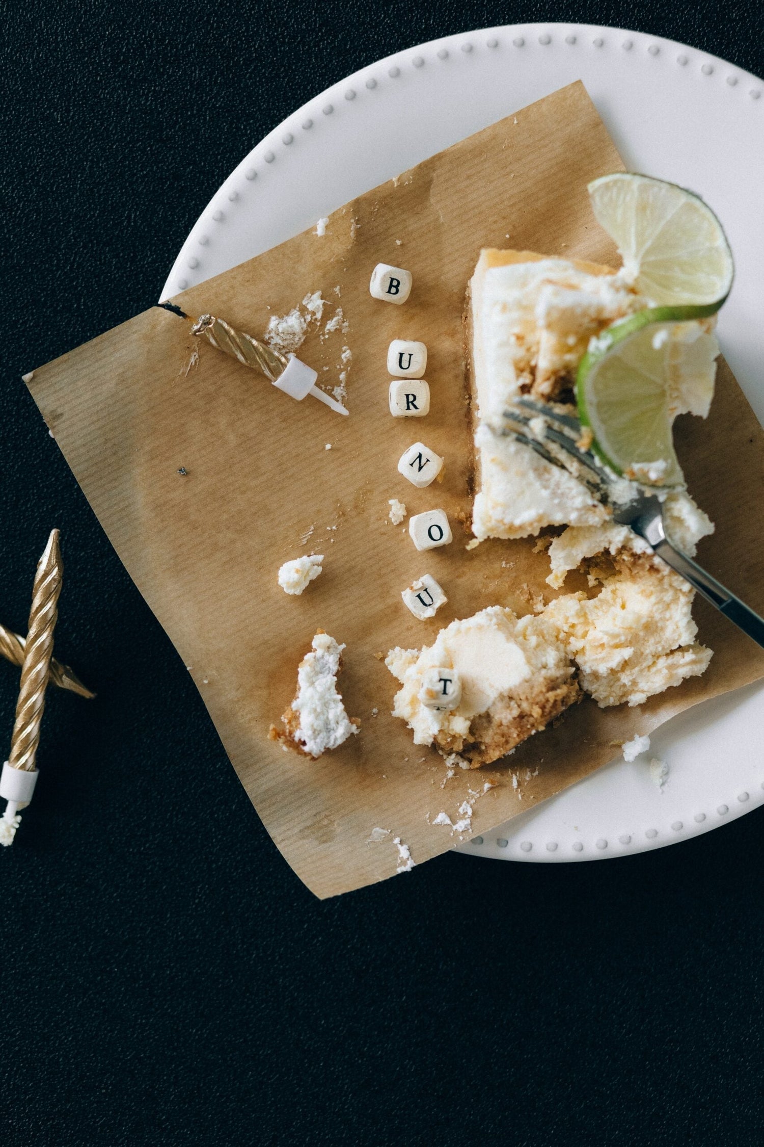 Overhead of partially eaten lime topped cheesecake with crumbs and letter cubes spelling BURNOUT on brown paper