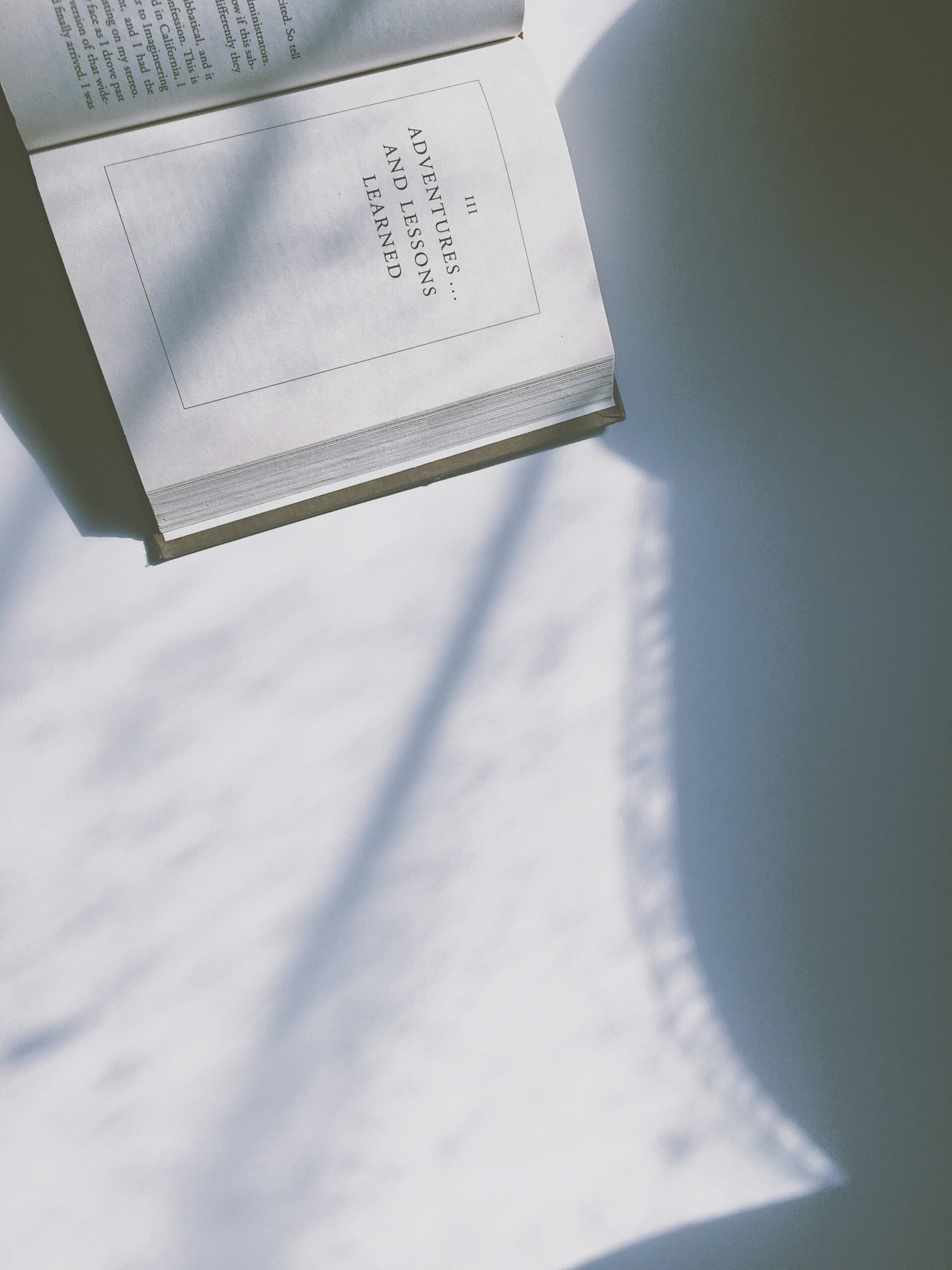 Open book showing page titled ‘Adventures and Lessons Learned’ resting on a table with soft window-shadow pattern