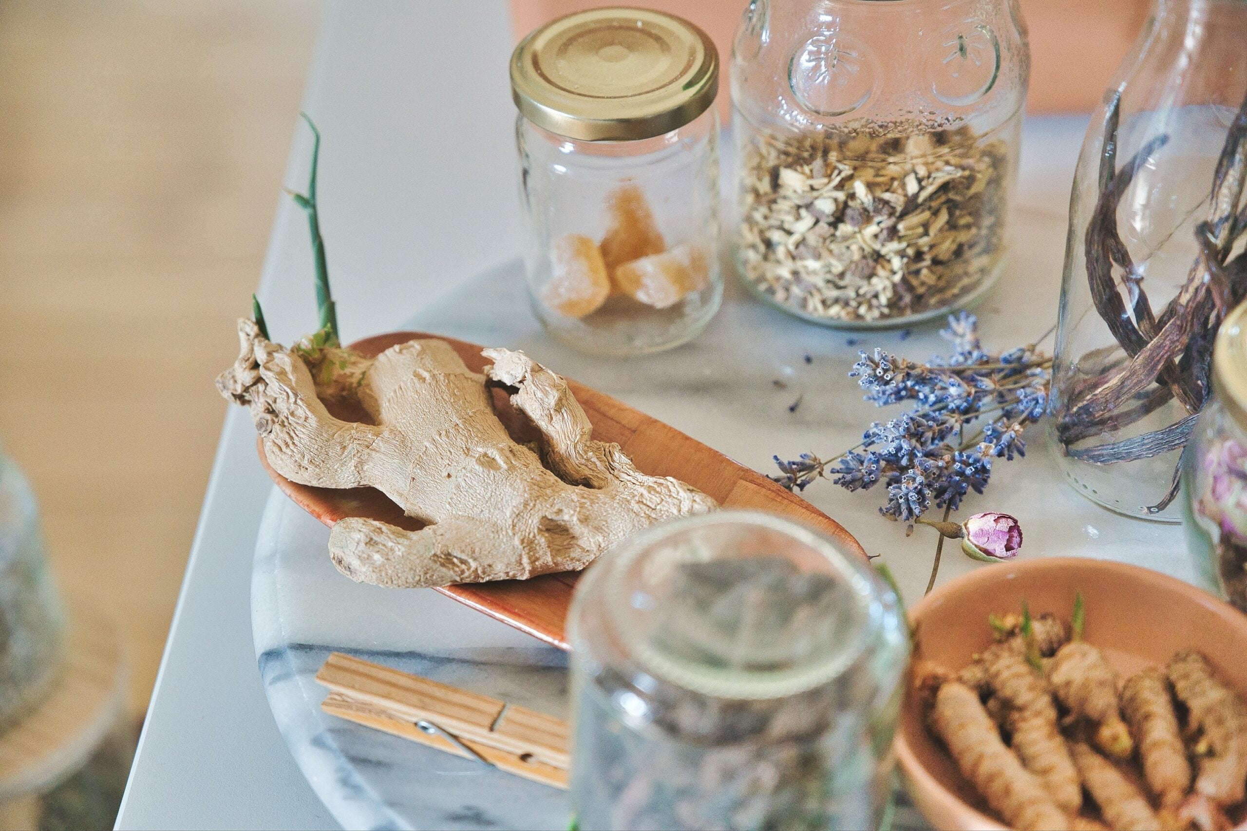 Ginger root and dried turmeric in bowls with glass jars and a sprig of lavender on a marble tabletop