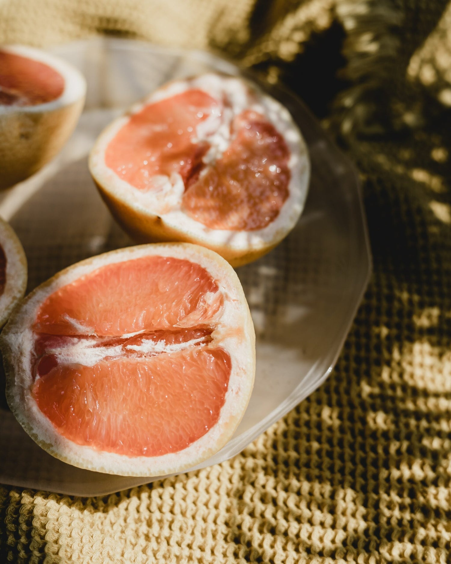 Halved pink grapefruit resting on a glass plate over a textured yellow cloth