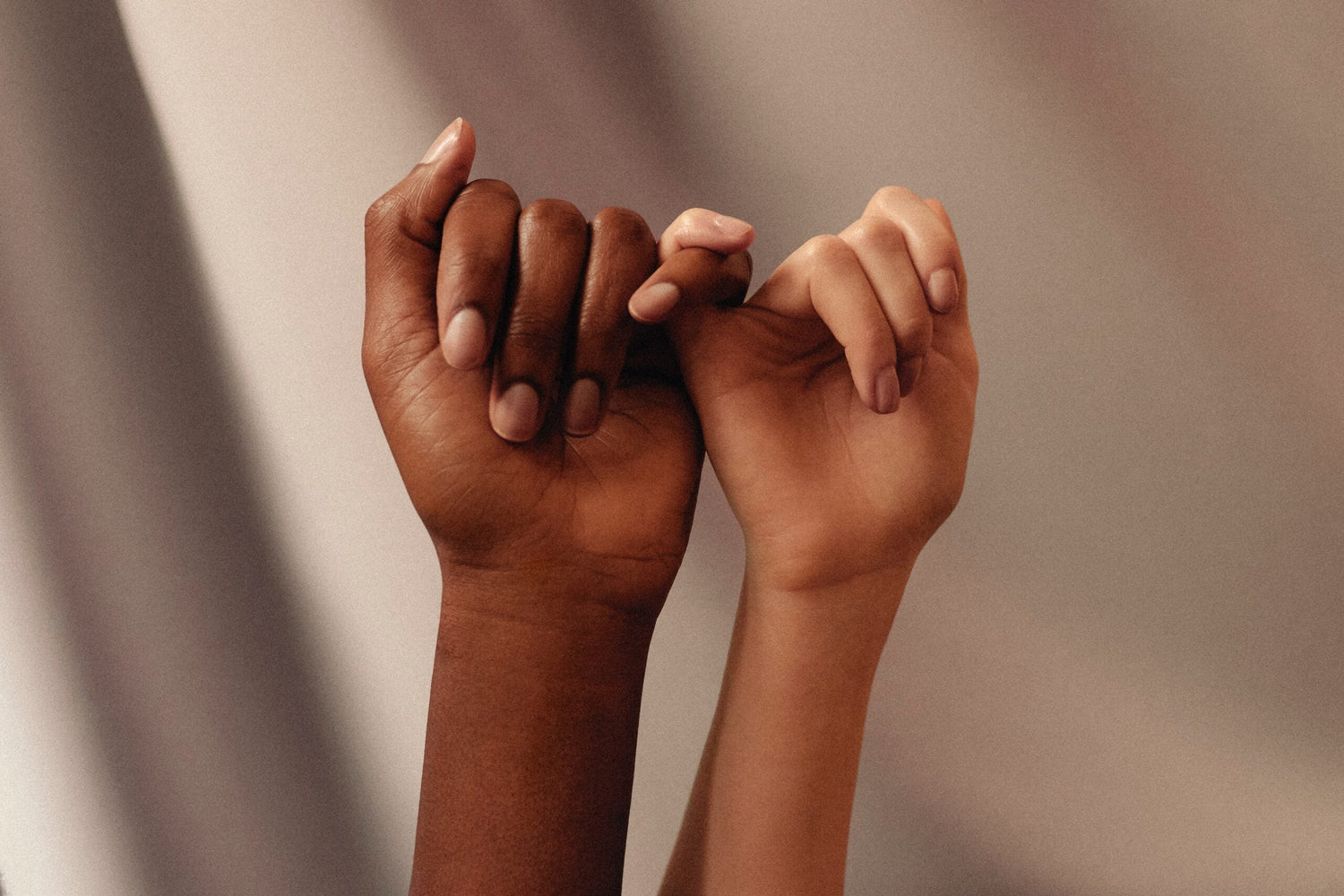 Two hands linking pinkies in a supportive gesture against a soft neutral background