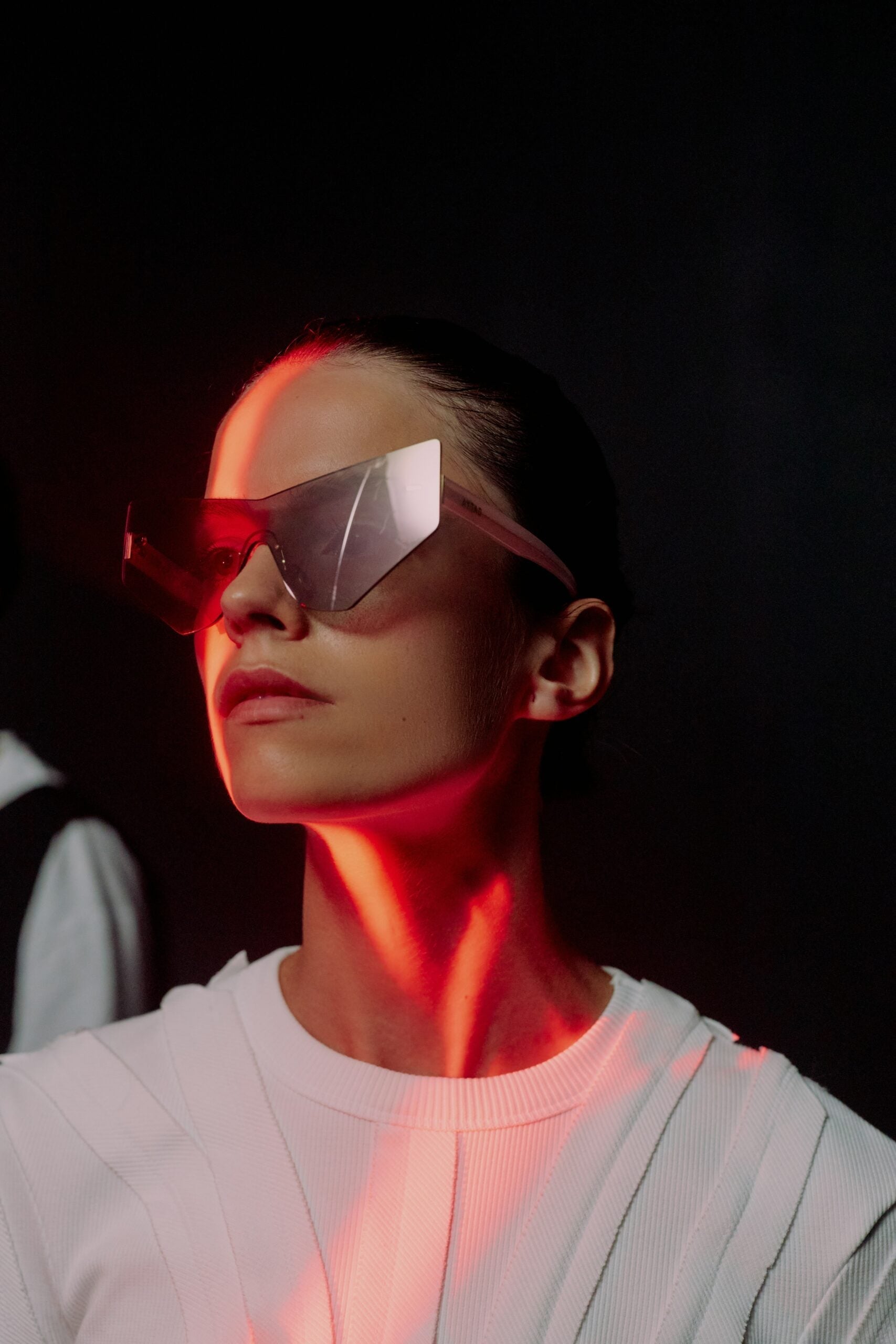 Woman wearing large protective goggles as a red infrared light illuminates her face and neck against a dark background
