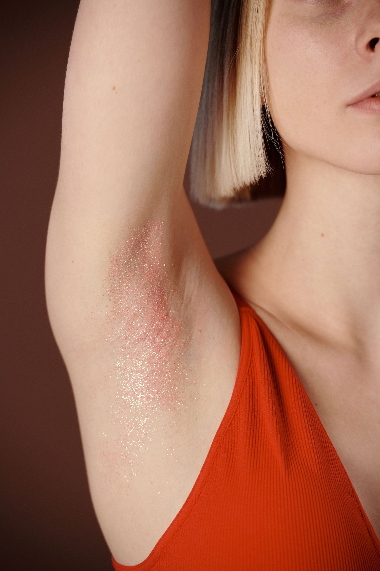 Close-up of raised underarm with pink clay detox residue and fine glitter, model wearing a red sleeveless top