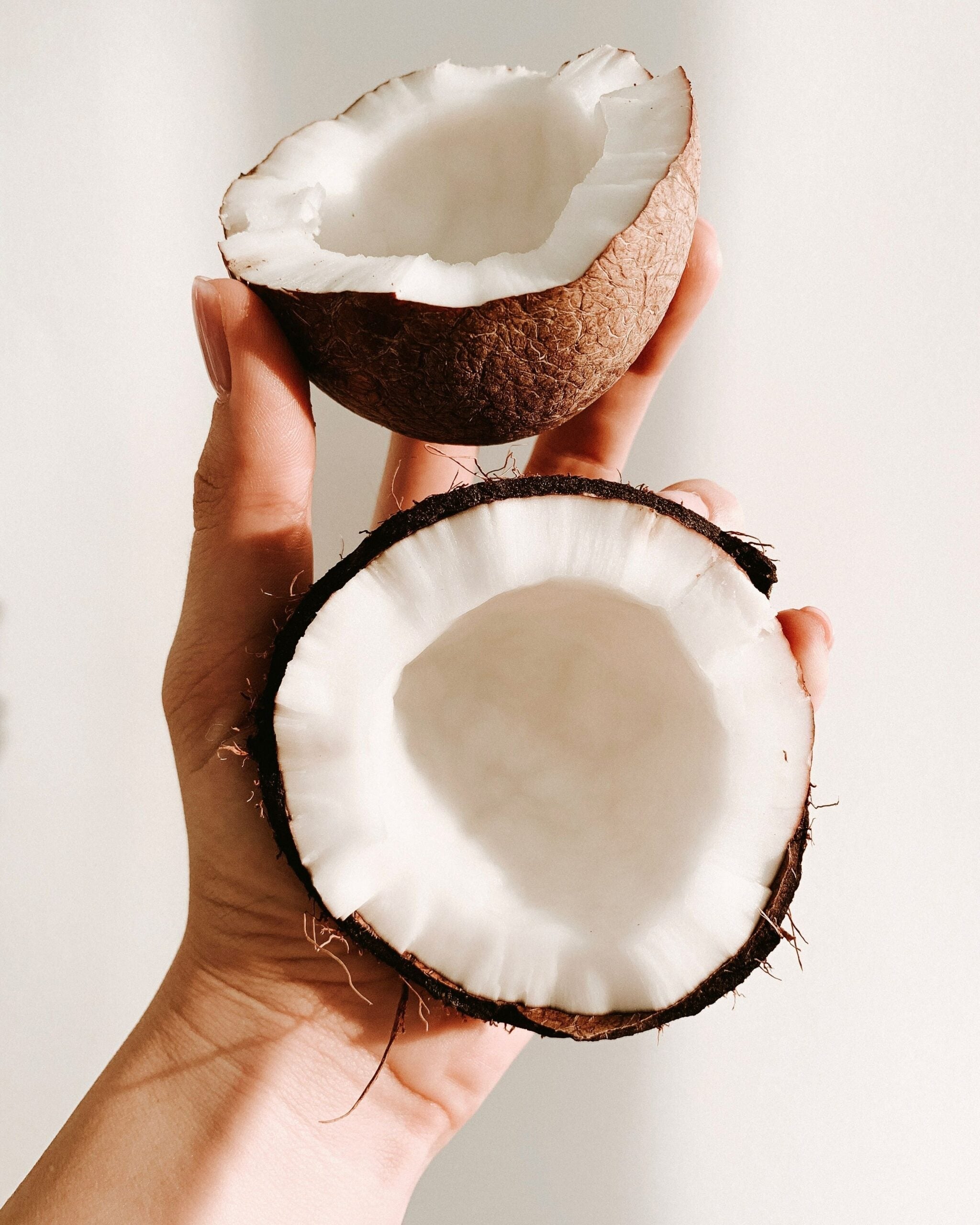 Hand holding two empty coconut halves against a pale background
