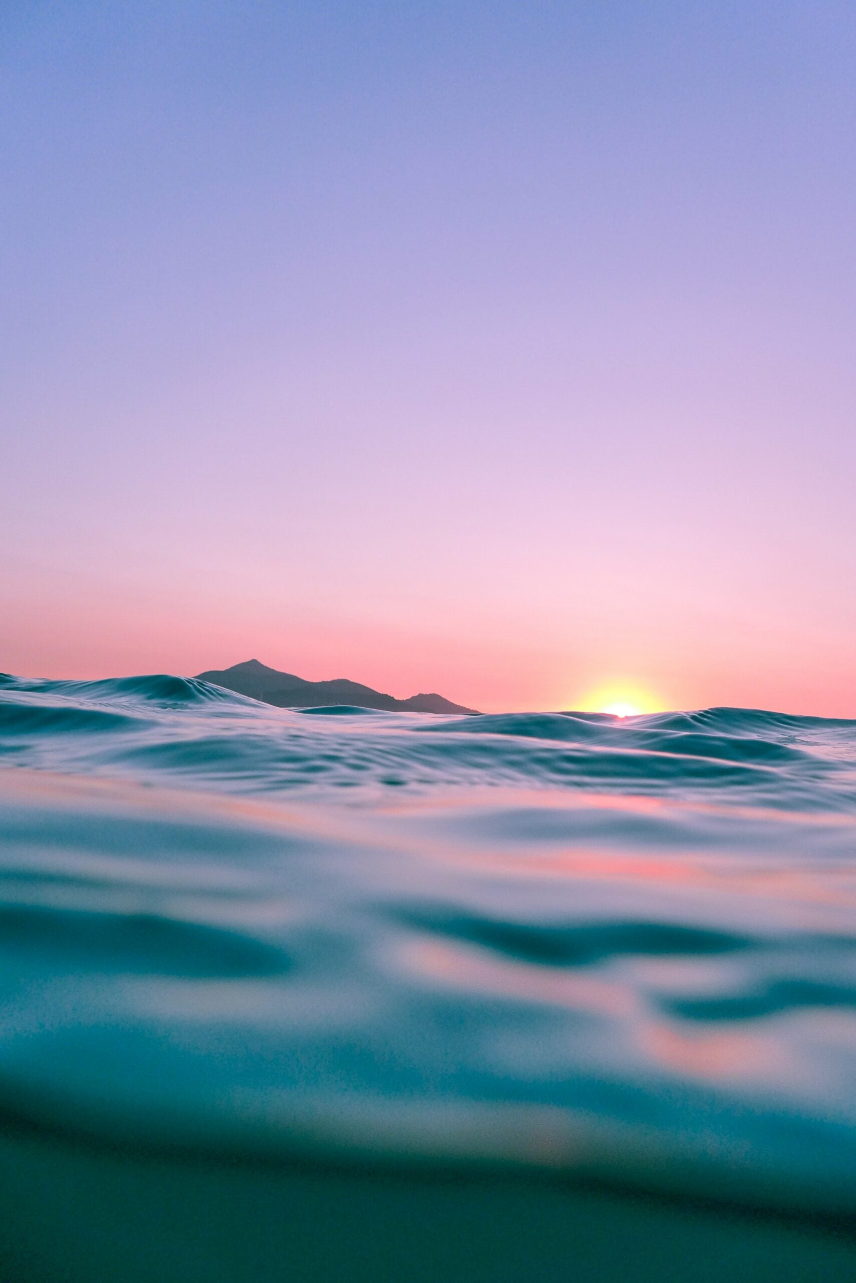 Sunrise peeking over a distant island with calm ocean waves in the foreground