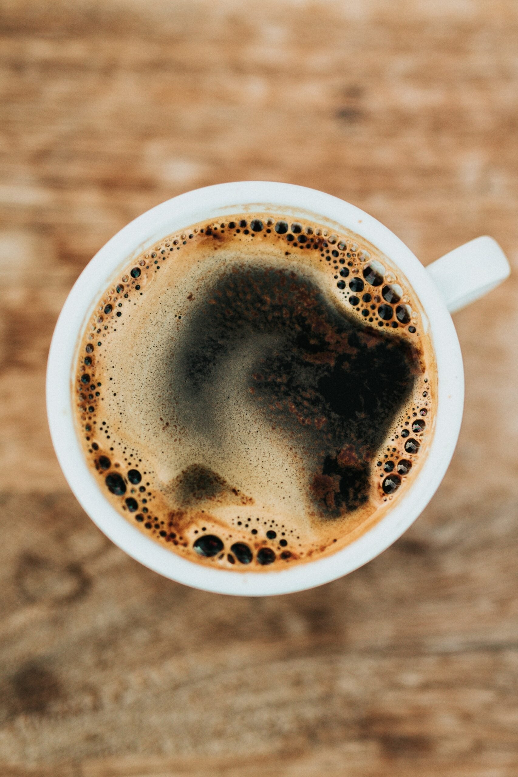 Overhead view of a white cup of black coffee with crema on a wooden table