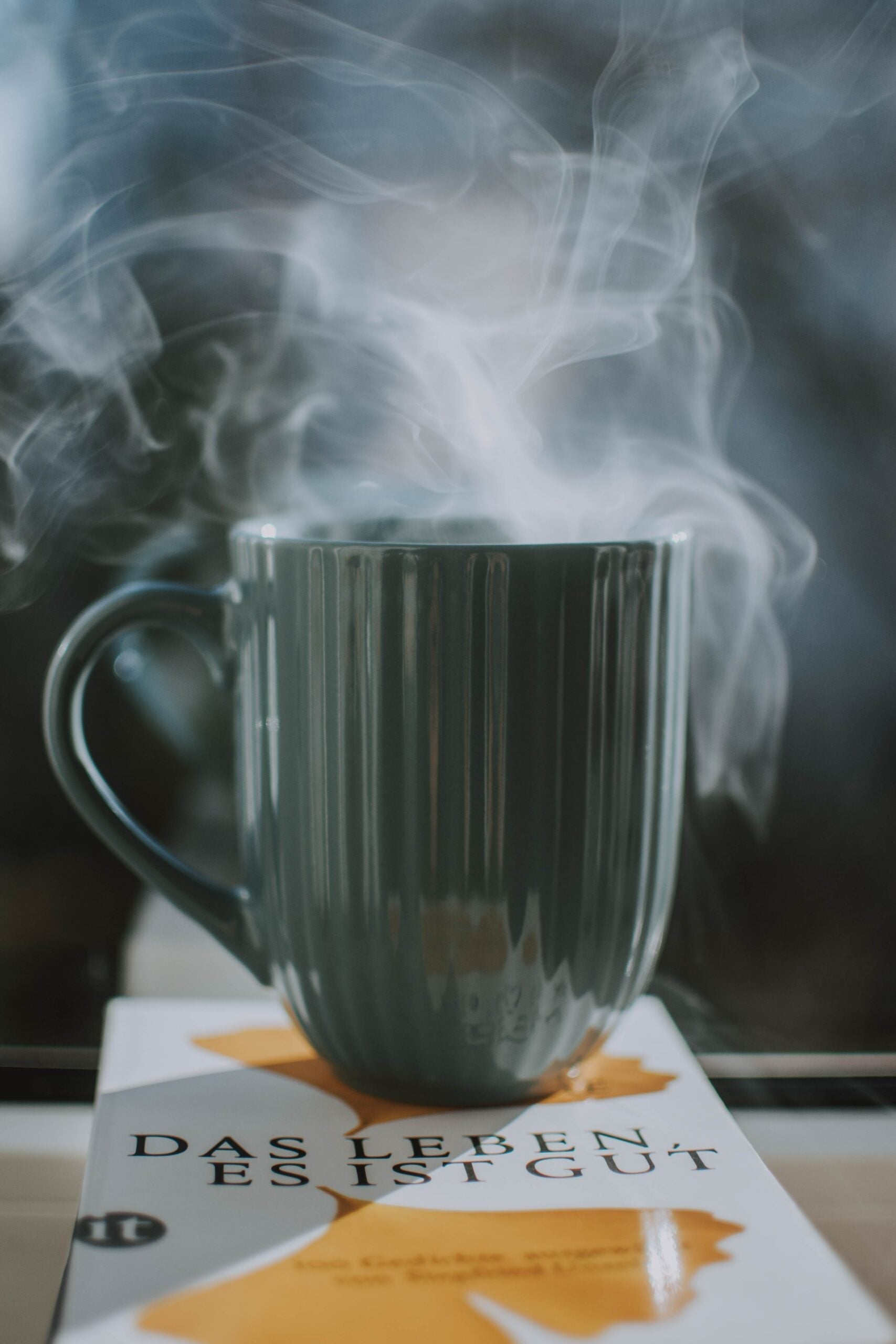 Steaming dark green ceramic mug releasing wisps of steam on a book in soft natural light