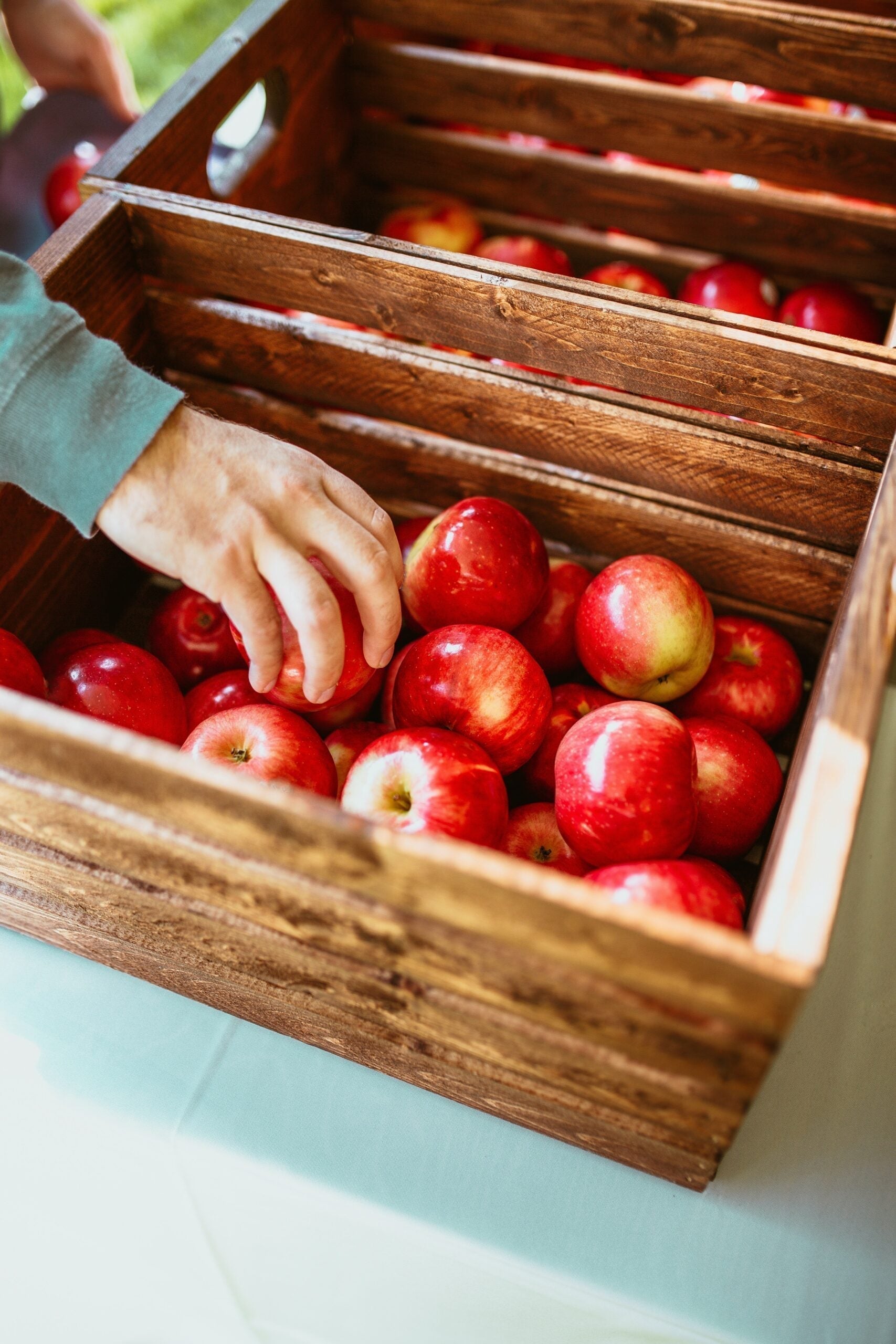 Hand picking a red apple from a wooden crate at a market