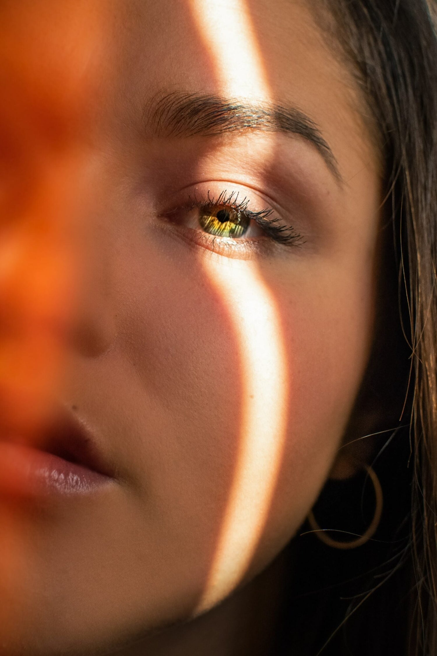 Close-up of a young woman’s face with a band of sunlight across her green eye, pensive mood
