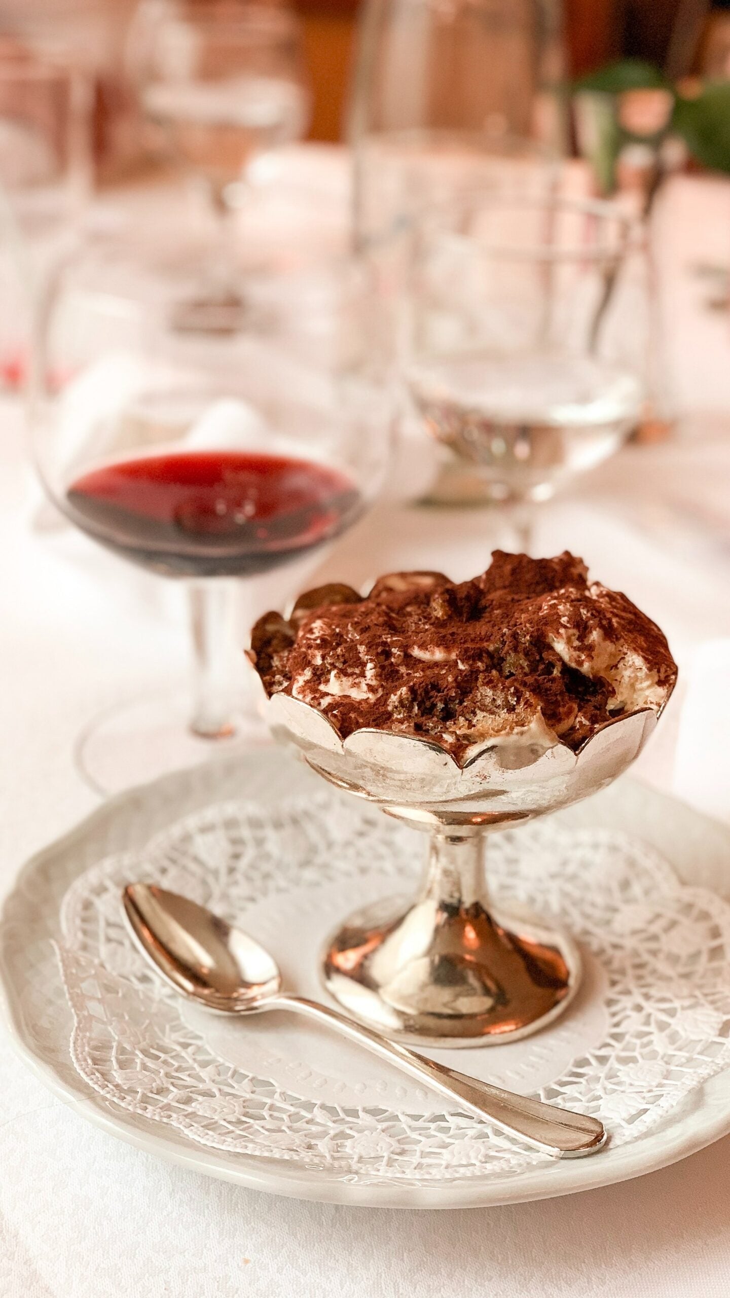 Chocolate-cocoa layered dessert in a silver compote with spoon on lace doily and a glass of red wine