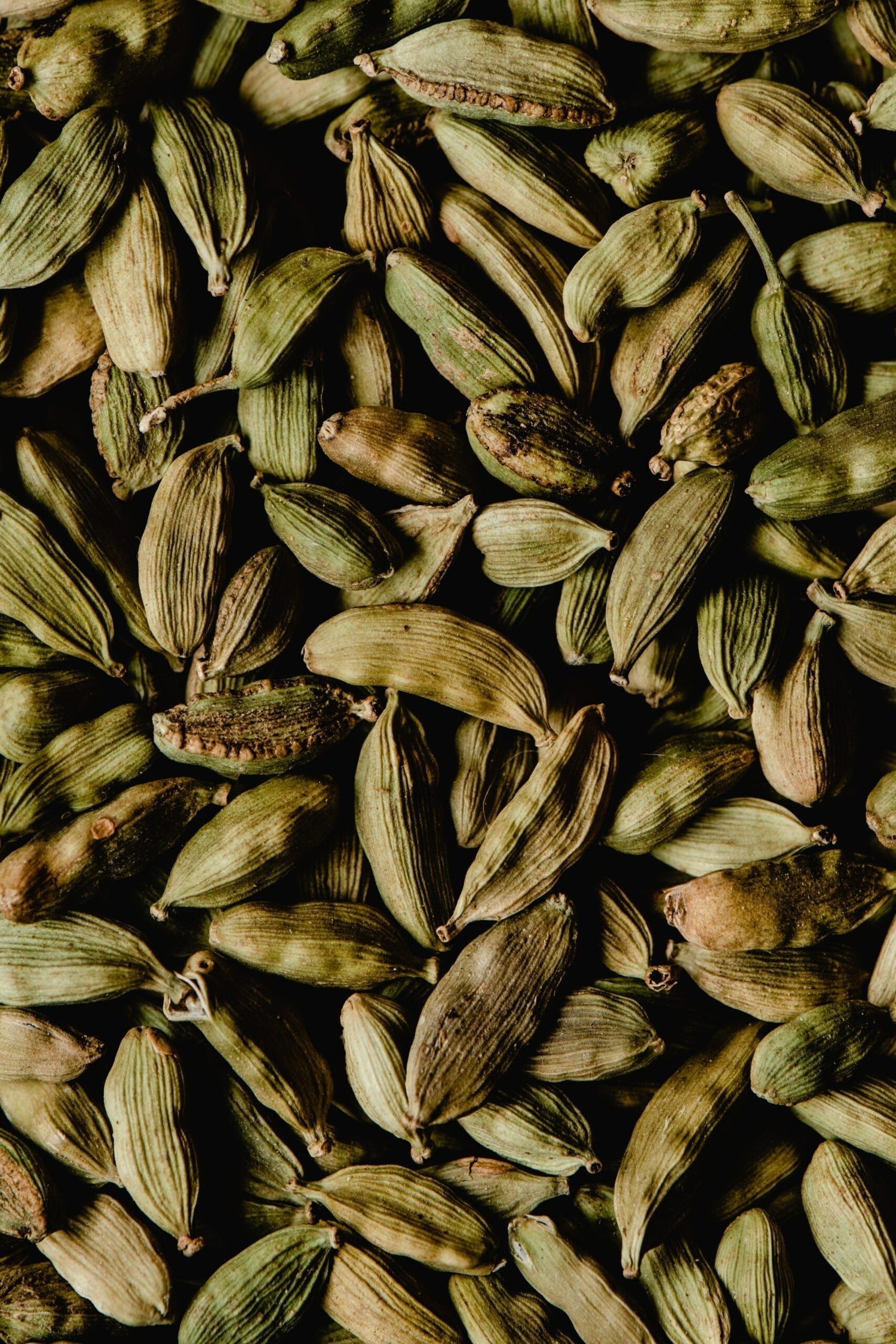 Close-up of green cardamom pods showing ridged husks and seeds against a dark background