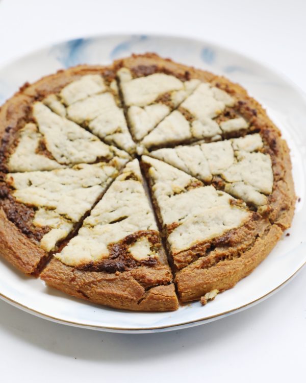 Overhead view of a sliced plantain pizza crust showing golden-brown edges and a creamy white topping on a white plate