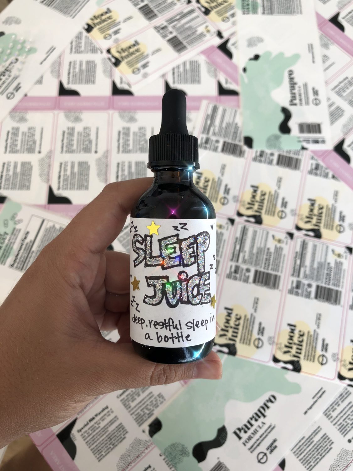 Hand holding Sleep Juice bottle, label reads ‘SLEEP JUICE’ and ‘deep, restful sleep in a bottle’ over printed labels