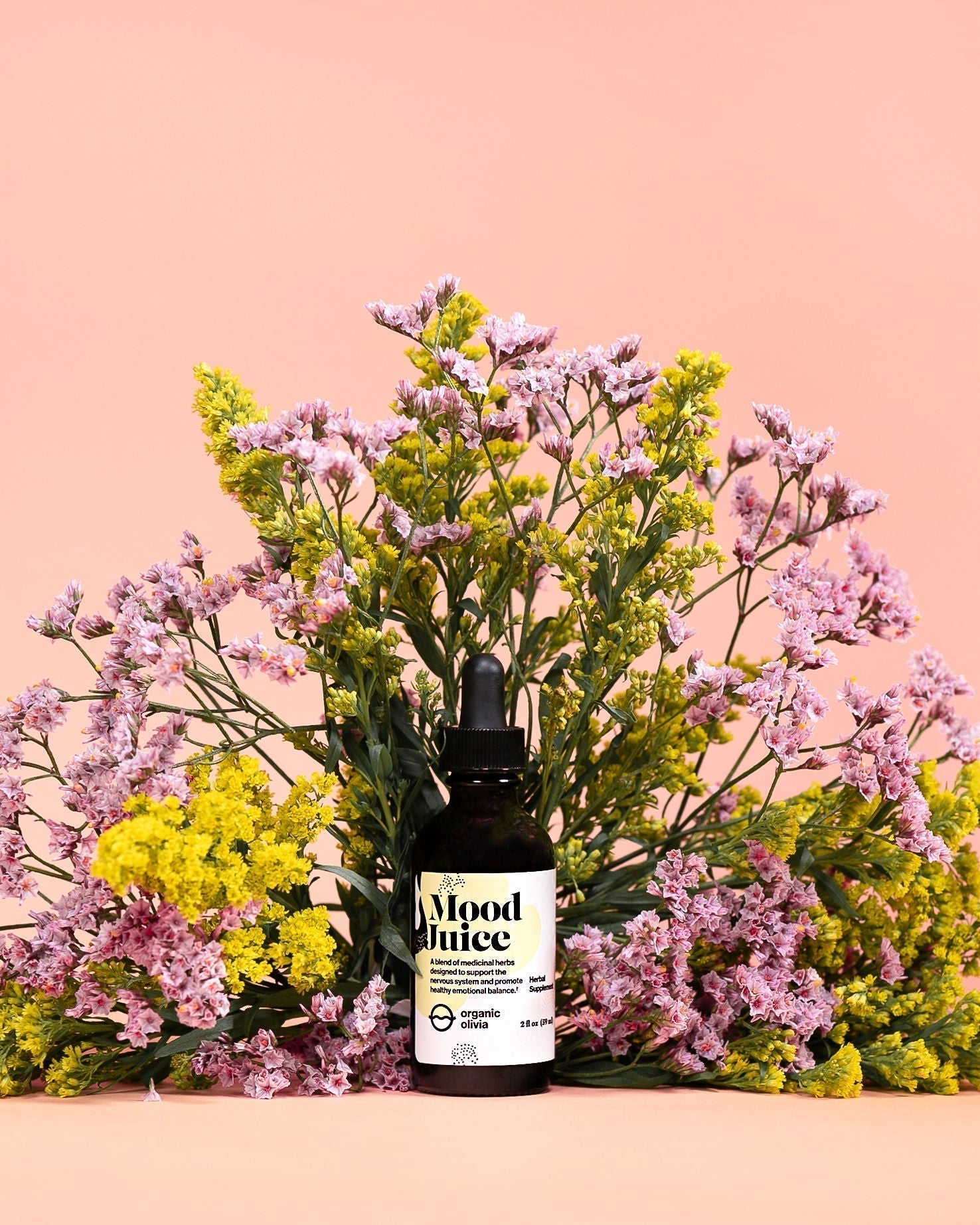 Front view of Mood Juice dropper bottle showing Mood Juice label, surrounded by pink and yellow flowers on a peach background