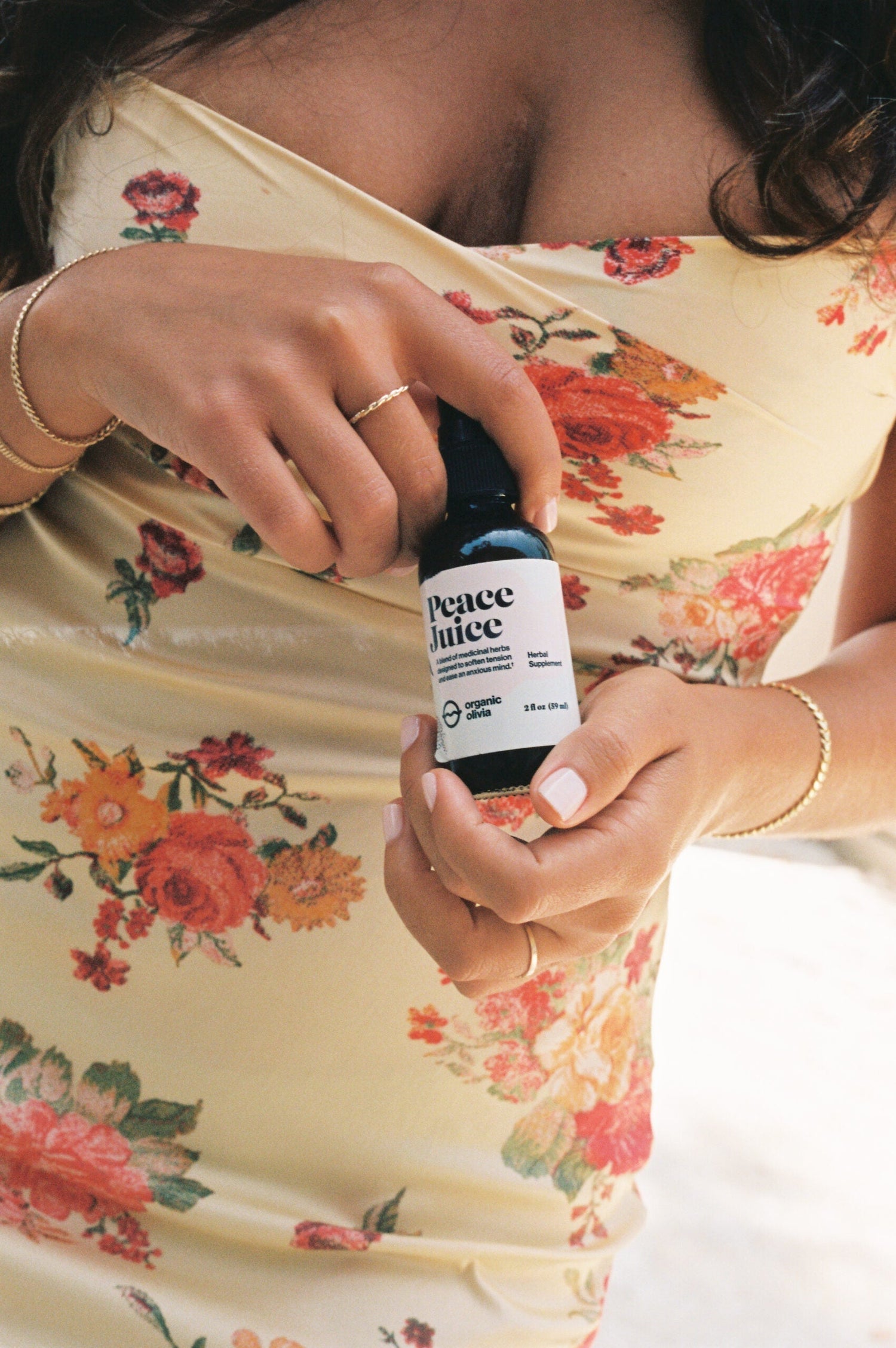 Woman holding Peace Juice herbal supplement dropper bottle while wearing a yellow floral dress