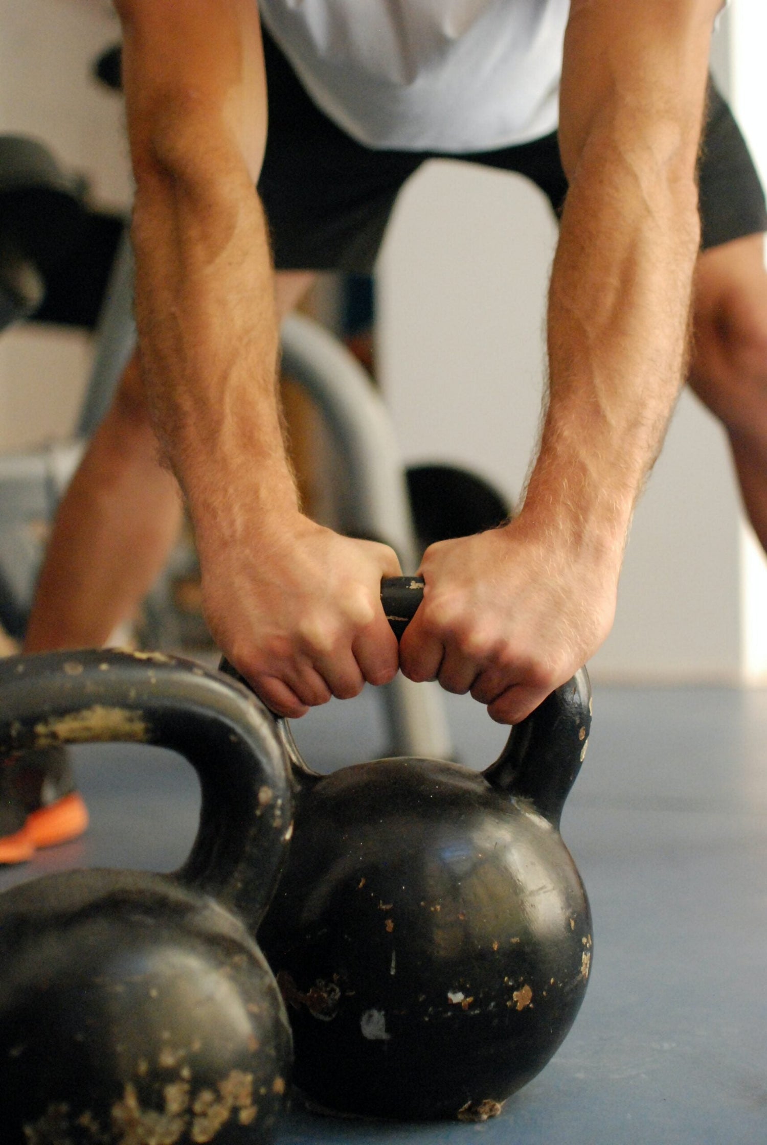 Close-up of a person gripping two kettlebell handles preparing to lift in a gym