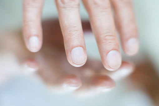 Close-up of three pale fingernails resting above a reflective surface