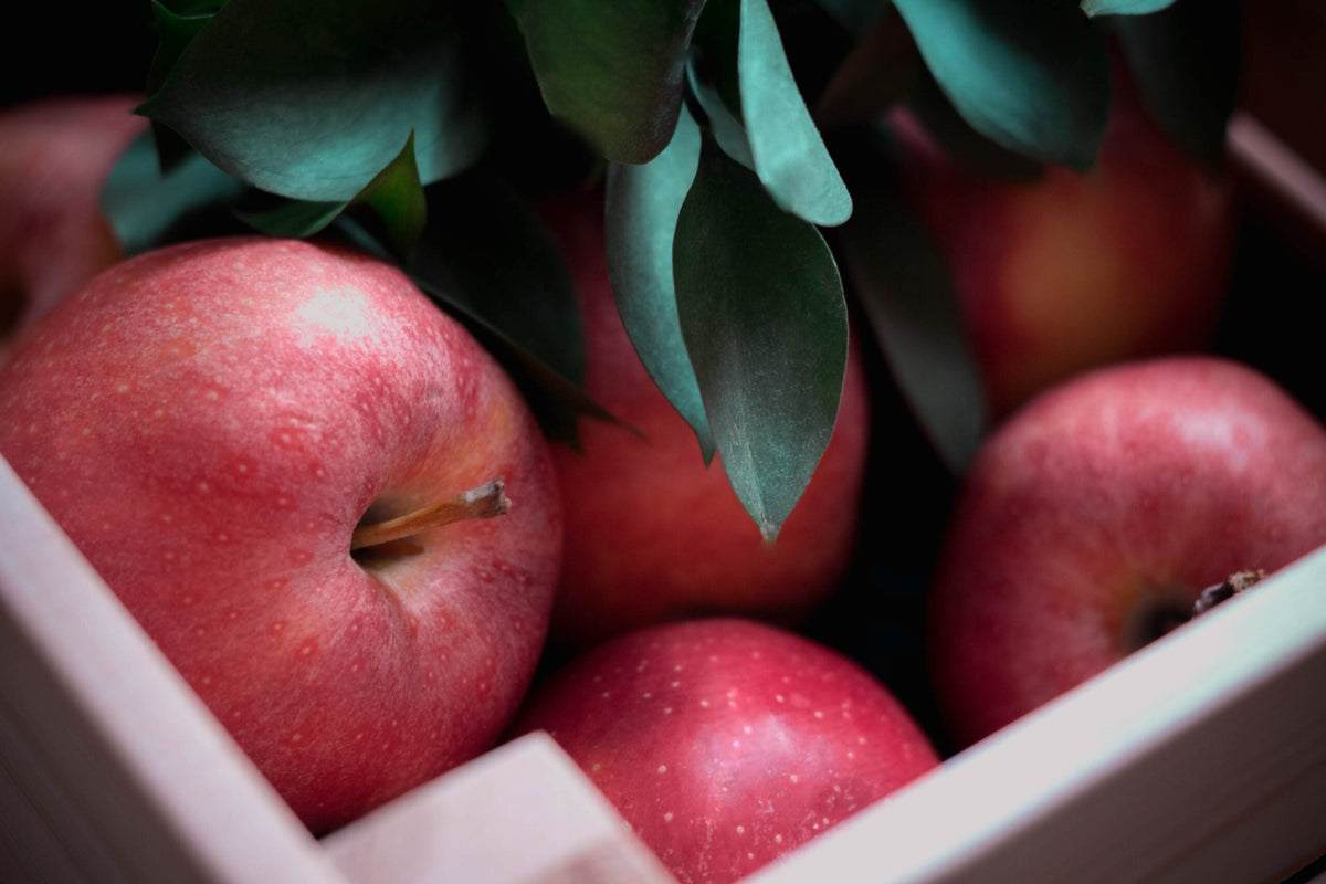 Close-up of red apples nestled in a wooden crate with green leaves