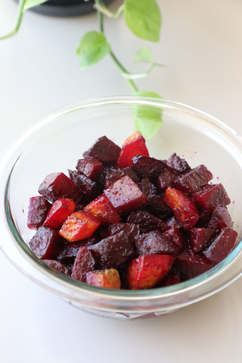 Roasted beet salad in a clear glass bowl on a white surface with a trailing green houseplant in the background