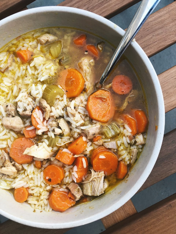 Bowl of chicken and rice soup with sliced carrots and celery, spoon resting in the bowl on a wooden table