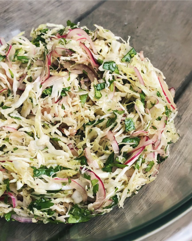 Bowl of shredded cabbage salad with thinly sliced red onion and chopped parsley on a wooden table
