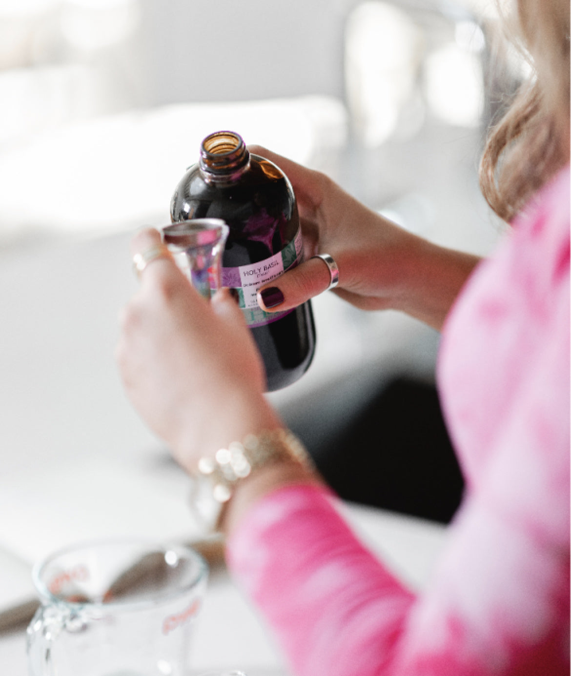 Person pouring herbal extract from a dark glass bottle into a small measuring cup at a bright kitchen counter