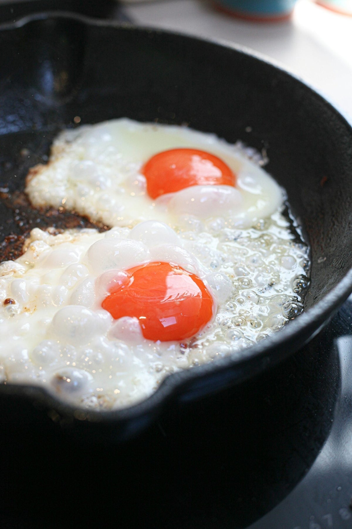 Two eggs frying in a cast-iron skillet with bright orange yolks and bubbling whites, close-up