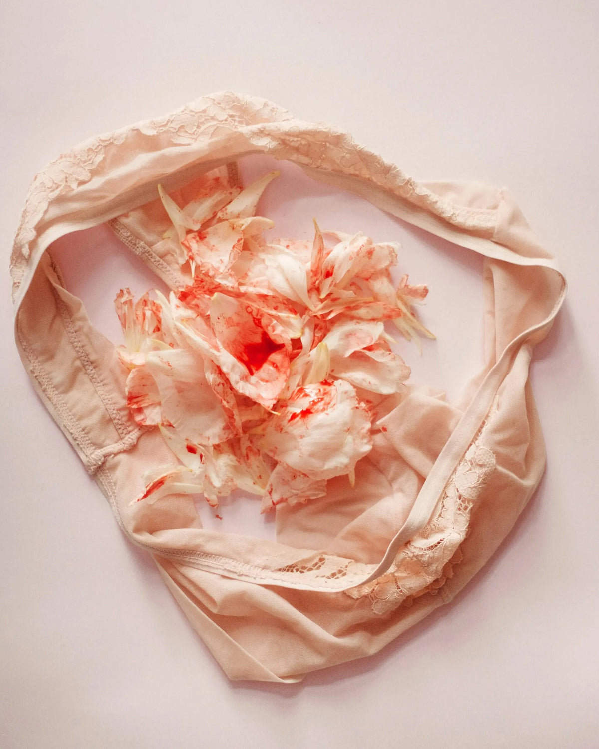 Lace underwear arranged with white flowers marked by red stains on a pale background