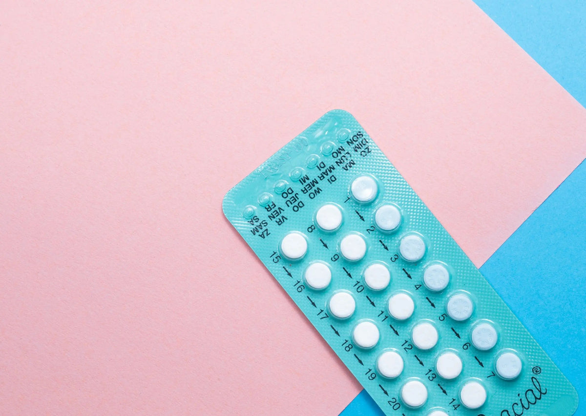 Angled top-right view of a teal blister pack of birth control pills showing numbered daily tablets on a pink and blue paper background