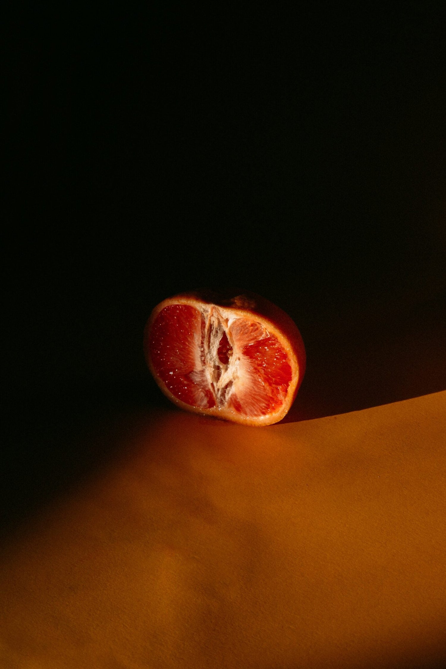 Halved blood orange resting on a mustard-colored surface in dramatic low light