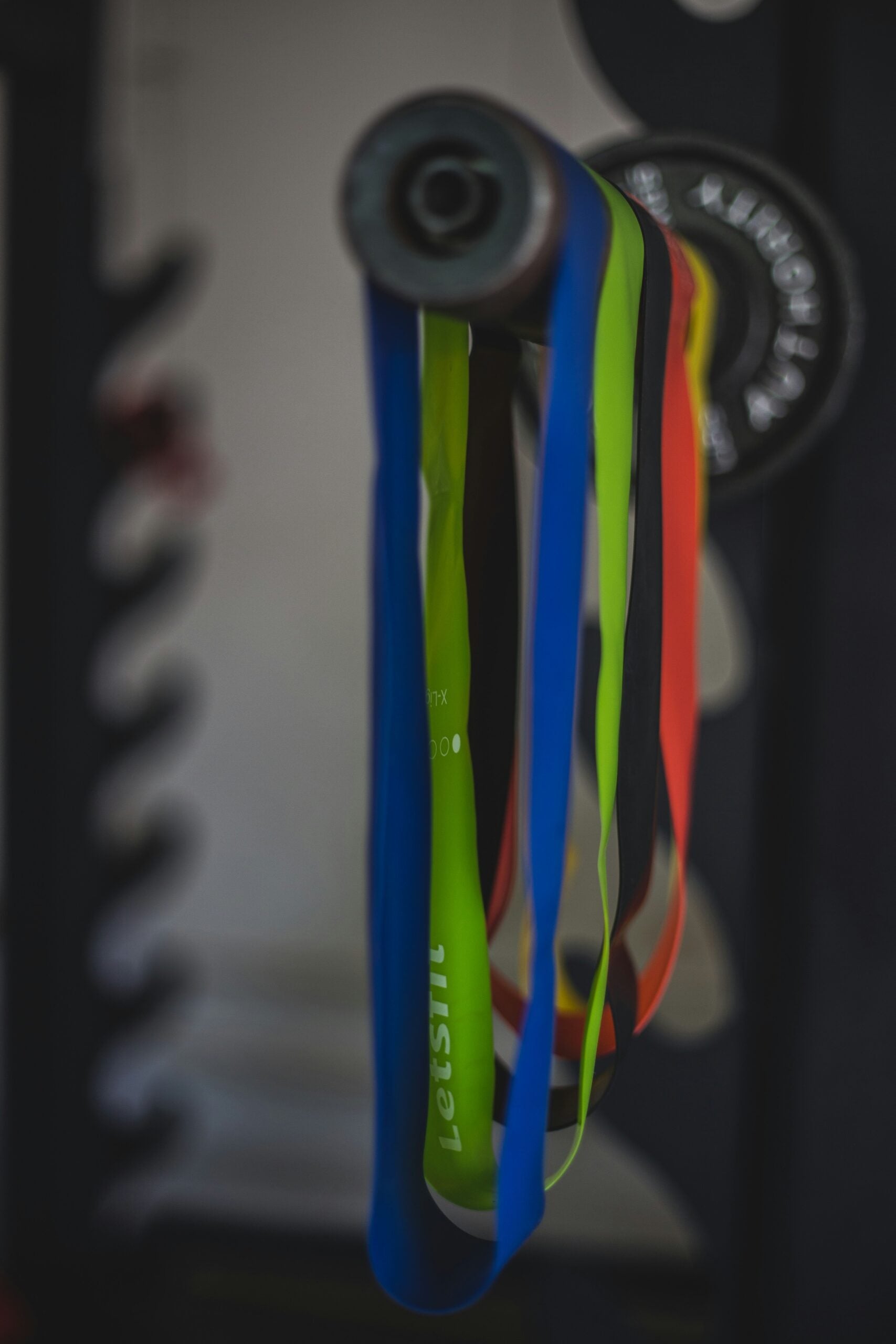 Colorful resistance bands hanging from a bar in a home gym with blurred weight plates in the background