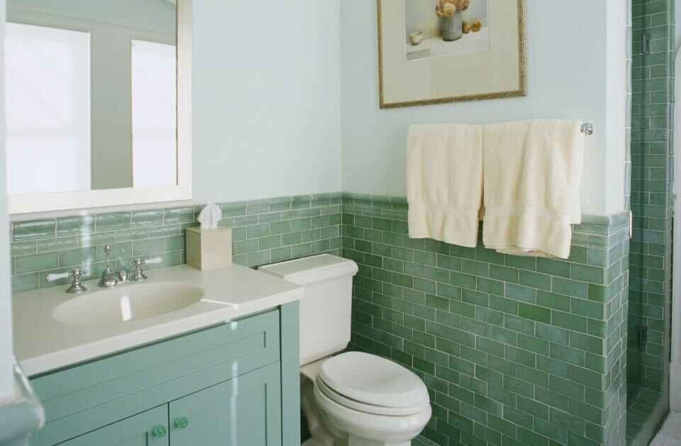 Bathroom featuring green subway-tiled half wall, mint vanity with sink, and white toilet in natural light