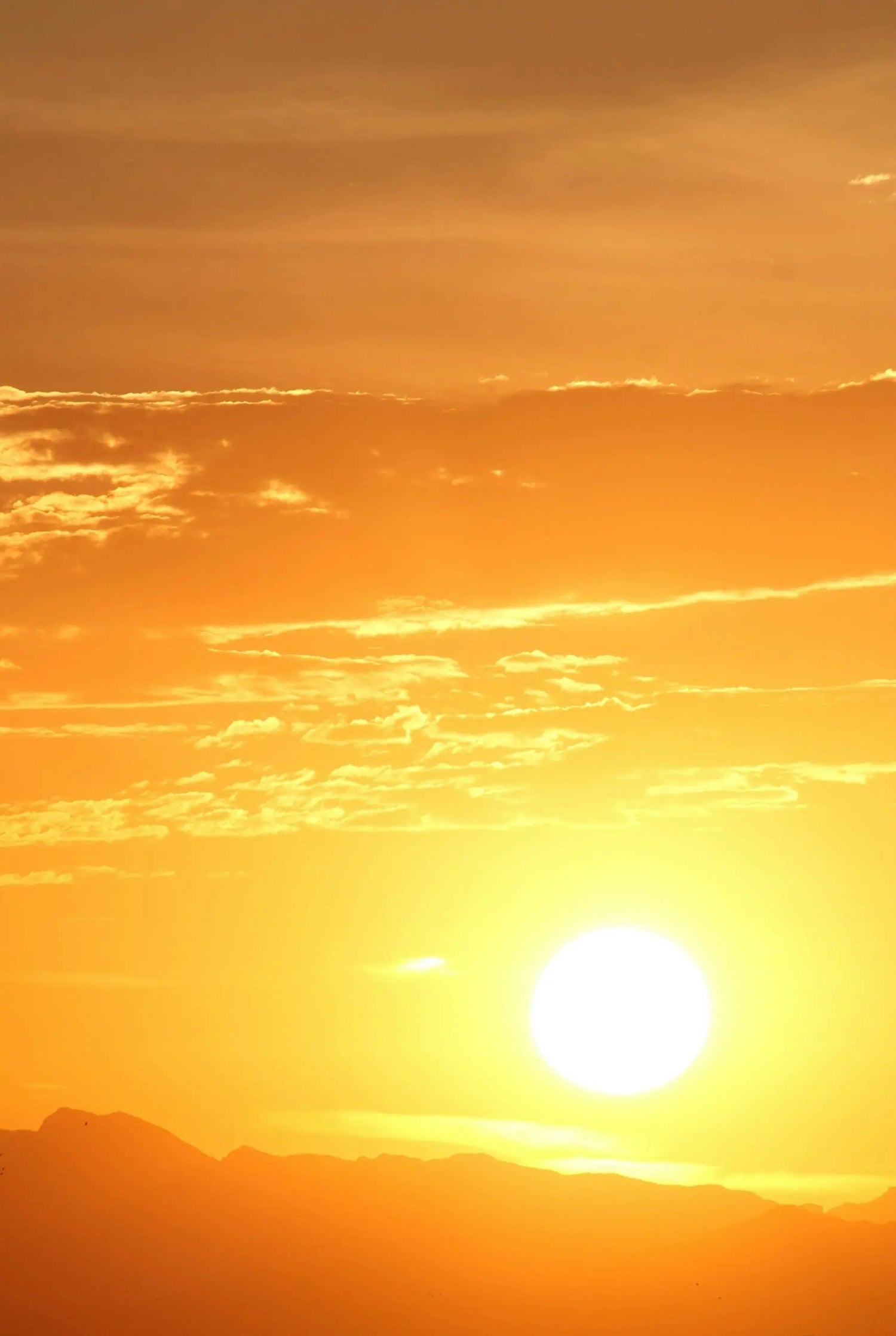 Sun setting over distant mountains with a golden sky and scattered clouds