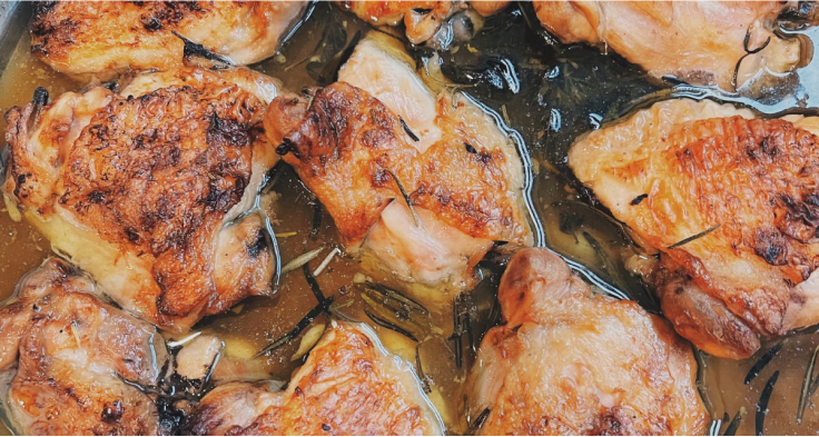 Close-up of baked lemon and rosemary chicken thighs simmering in a glossy herbed pan sauce
