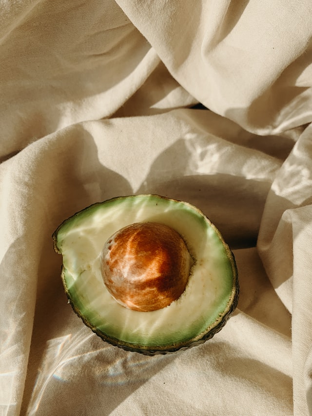 Half avocado with pit resting on crumpled beige linen in warm natural light