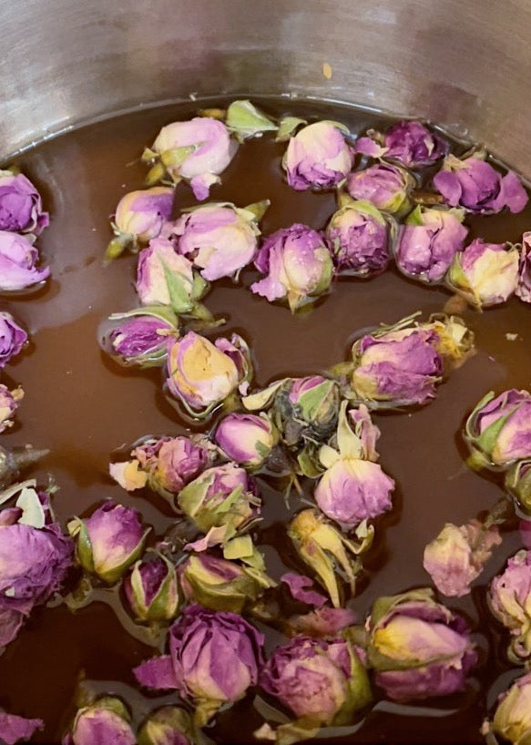 Rosebuds steeping in amber simple syrup in a stainless steel pot