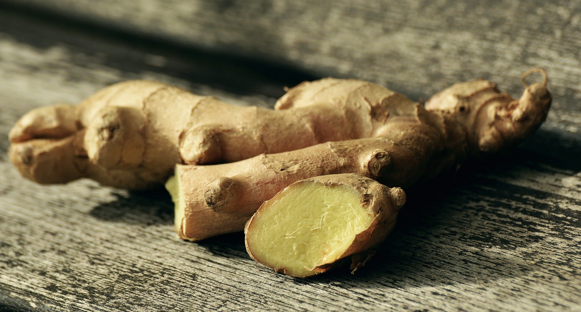 Close-up of ginger root showing knobbly brown skin and sliced pale yellow interior on a weathered wooden surface