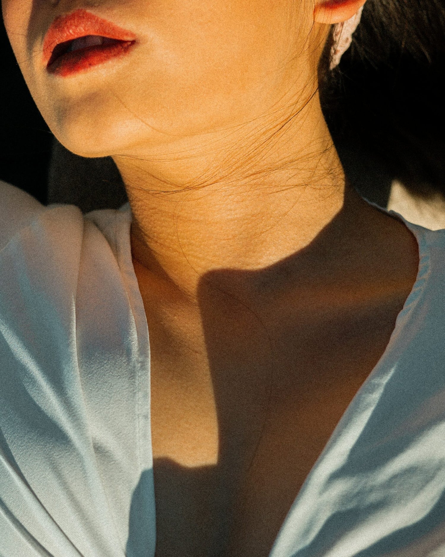 Close-up of a woman’s lower face and neck lit by warm sunlight, shadow across her collarbone and thyroid area