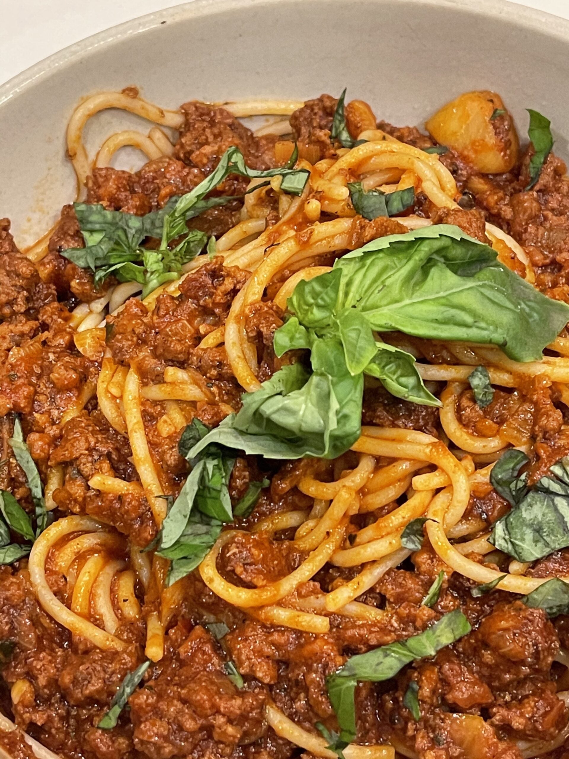 Spaghetti topped with spicy Spanish bolognese sauce, ground meat, and torn basil in a shallow white bowl