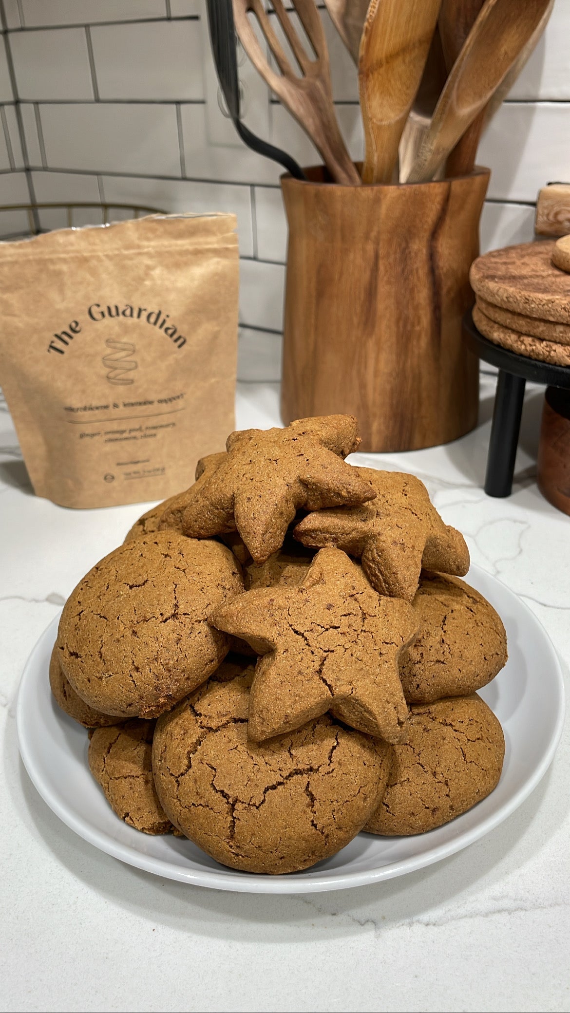Close-up of spiced sugar cookies showing cracked tops and star shapes with The Guardian tea pouch and wooden utensils in a tiled kitchen