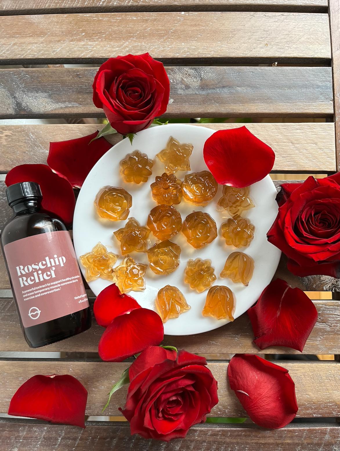 Plate of rosehip gummies arranged with bottle labeled Rosehip Relief and red rose petals on a wooden table