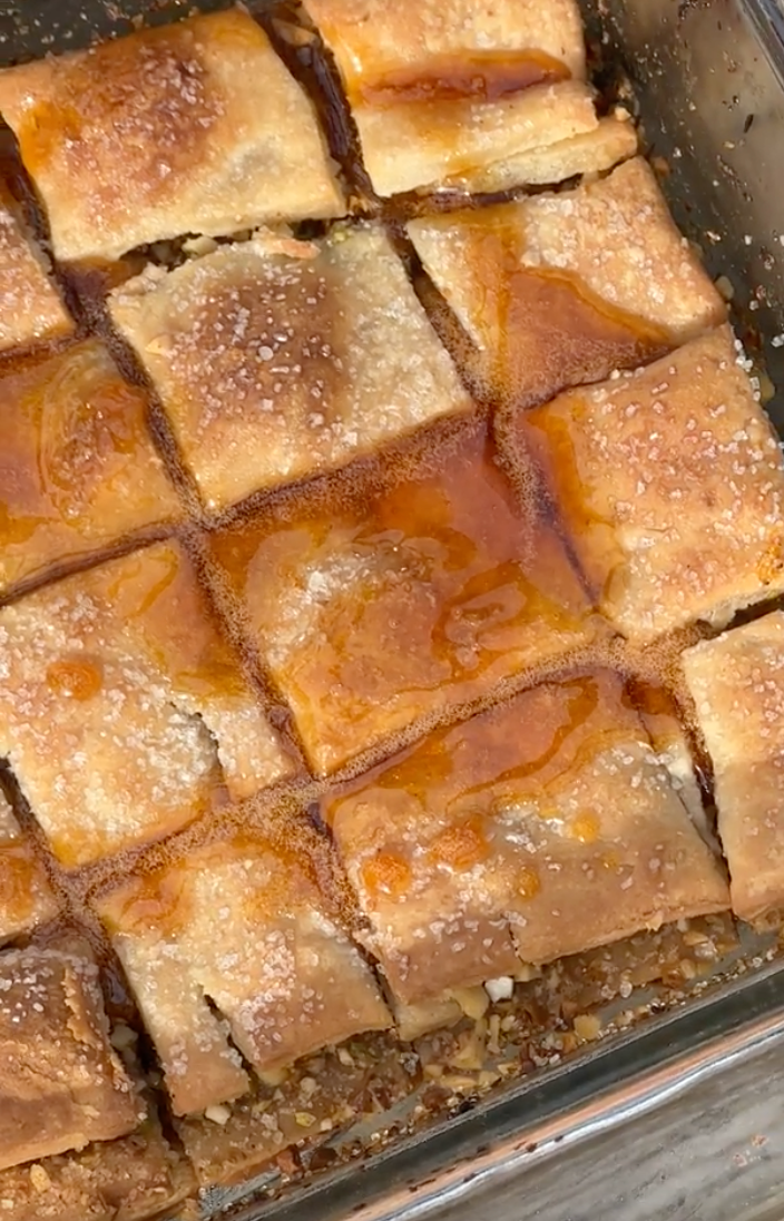 Close-up of gluten-free blood orange baklava showing flaky golden pastry, nut filling, and glossy blood-orange syrup in a glass baking dish