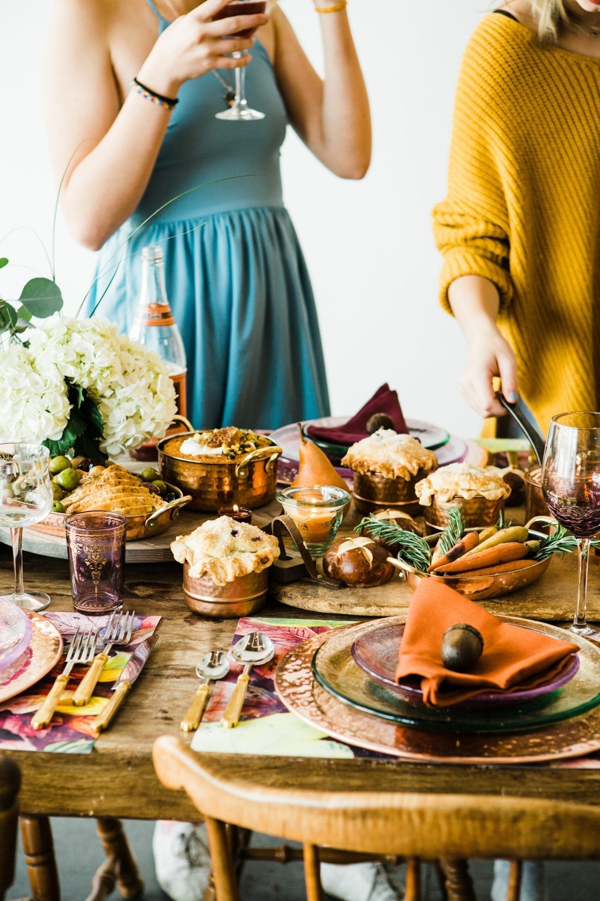 Two women gather around a richly set dining table with food, drinks, and flowers