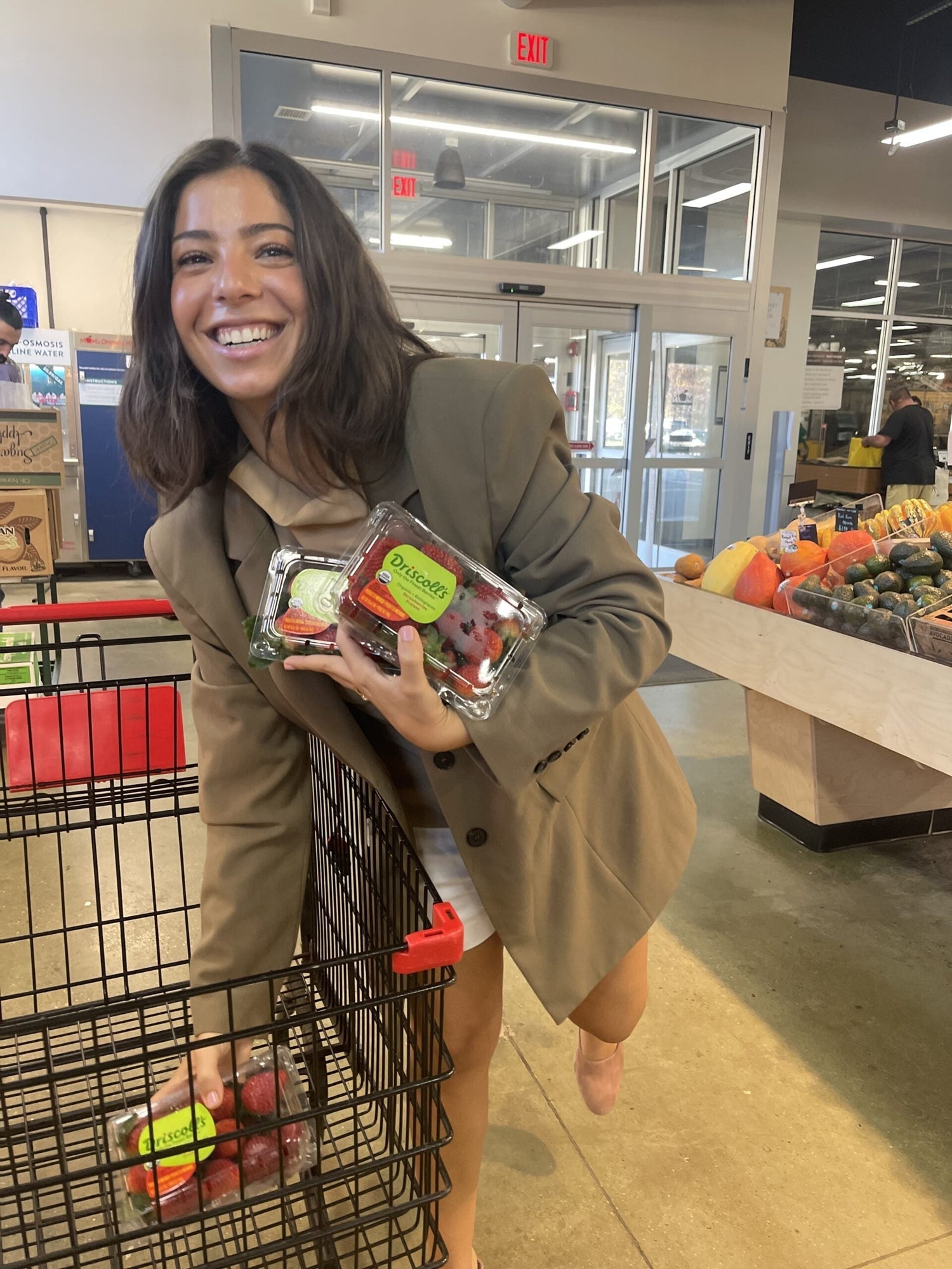Smiling woman grocery shopping holding packaged strawberries near the produce section