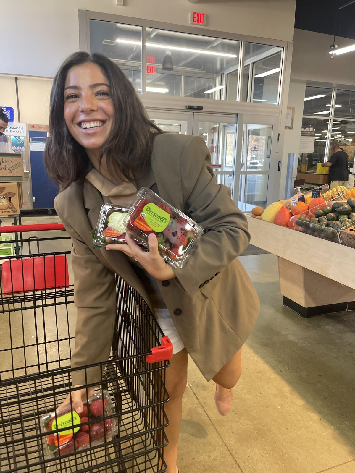 Smiling woman grocery shopping holding packaged strawberries near the produce section