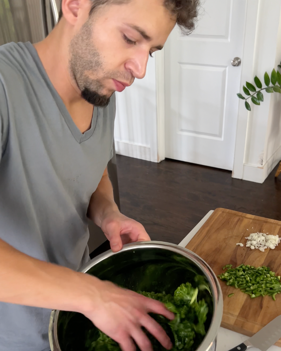 Person massaging kale in a stainless steel bowl in a home kitchen with chopped onion and jalapeño on a cutting board