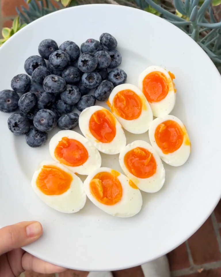 Soft-boiled eggs and blueberries arranged on a plate for breakfast outdoors
