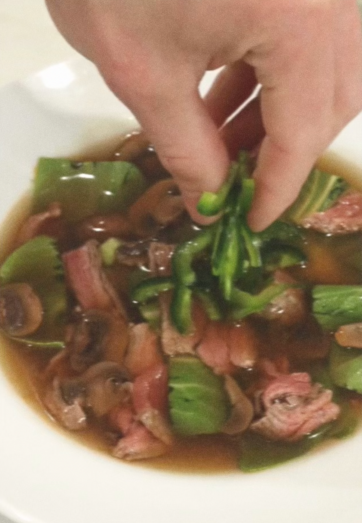 Hand placing sliced greens into a bowl of mushroom and steak soup