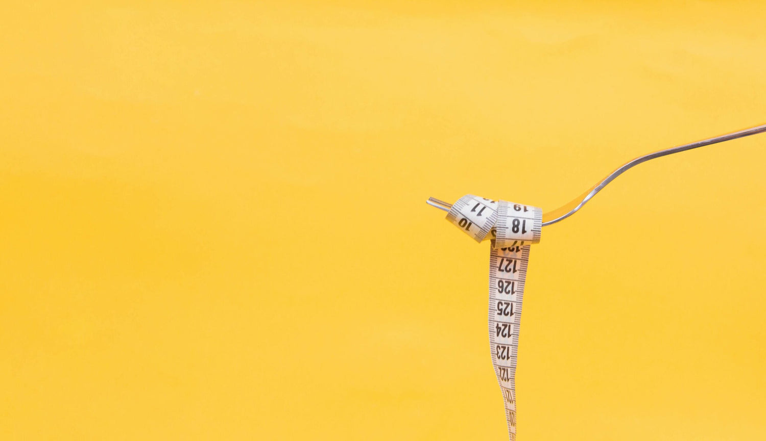 Fork holding a coiled measuring tape against a solid yellow background